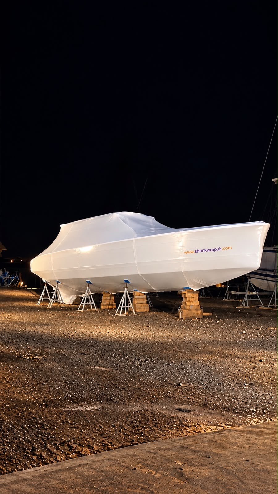 A 17 metre superyacht tender shrink wrapped and lit at night in a Scottish yard